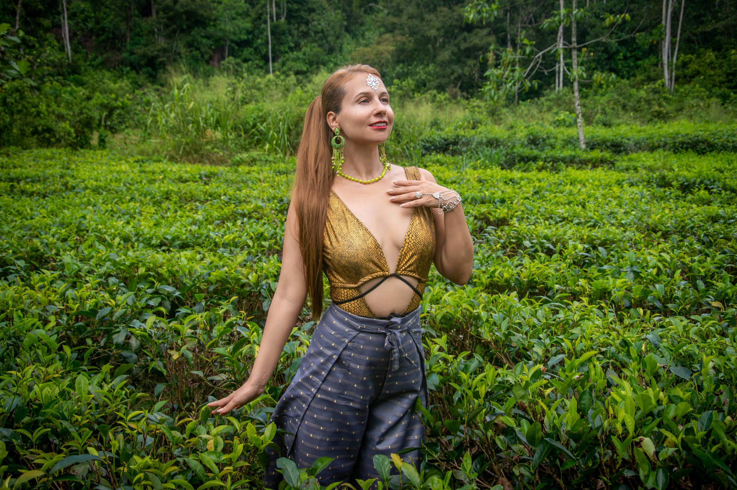 Woman wearing golden attire enjoying a lush green tea field, capturing nature's beauty and cultural elegance.
