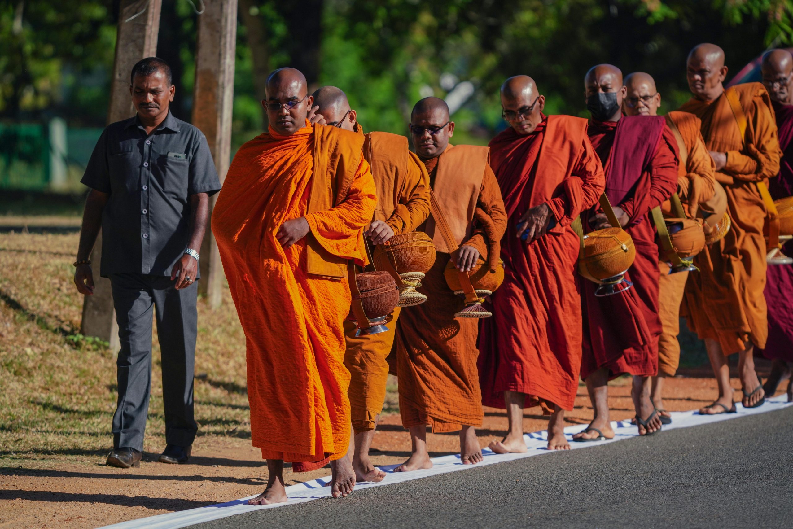 Buddhist monks in orange robes walk in a pilgrimage procession, showcasing a spiritual tradition in Sri Lanka.