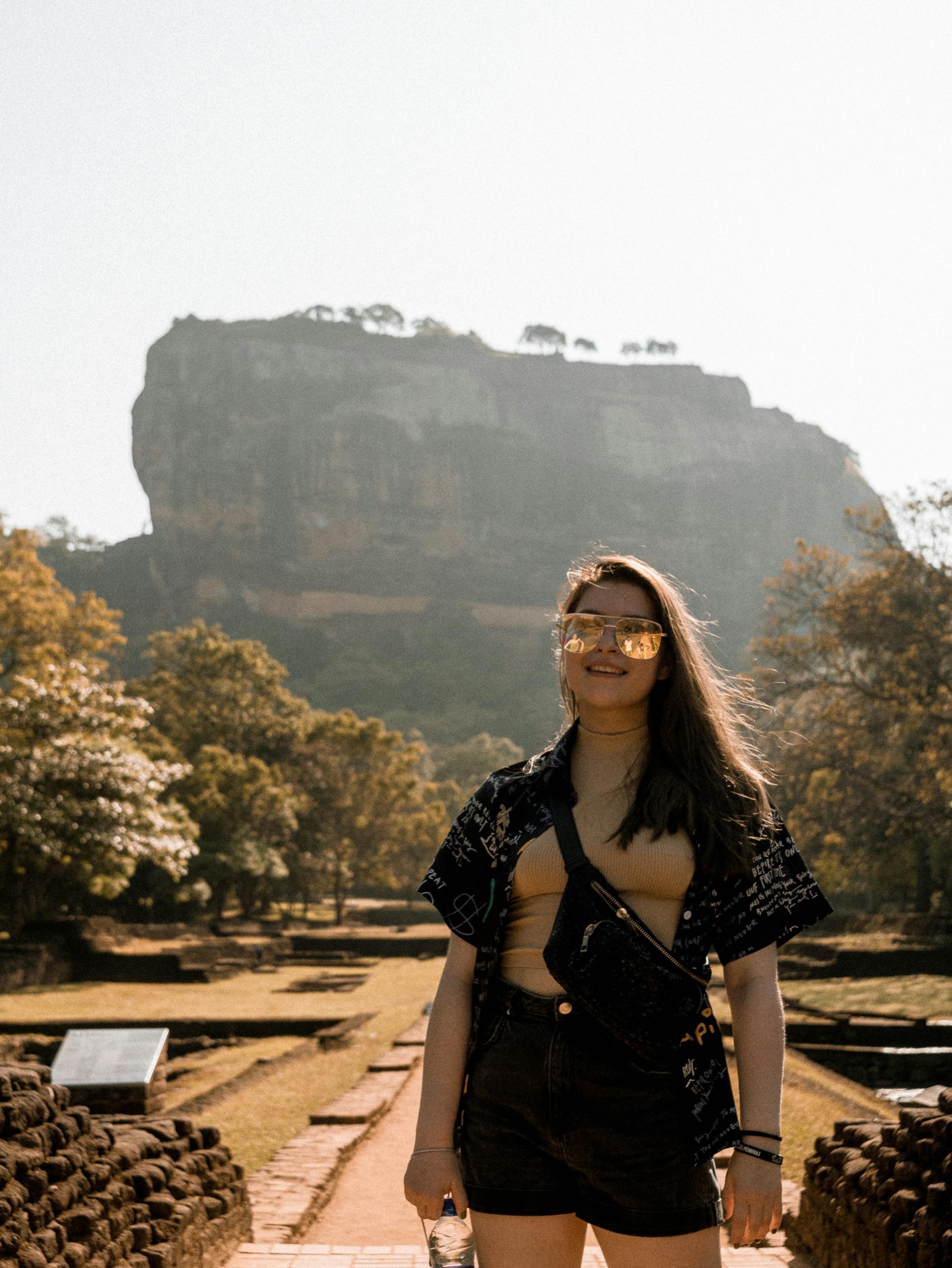 Young woman smiling in front of the iconic Sigiriya Rock Fortress in Sri Lanka, a popular travel destination.