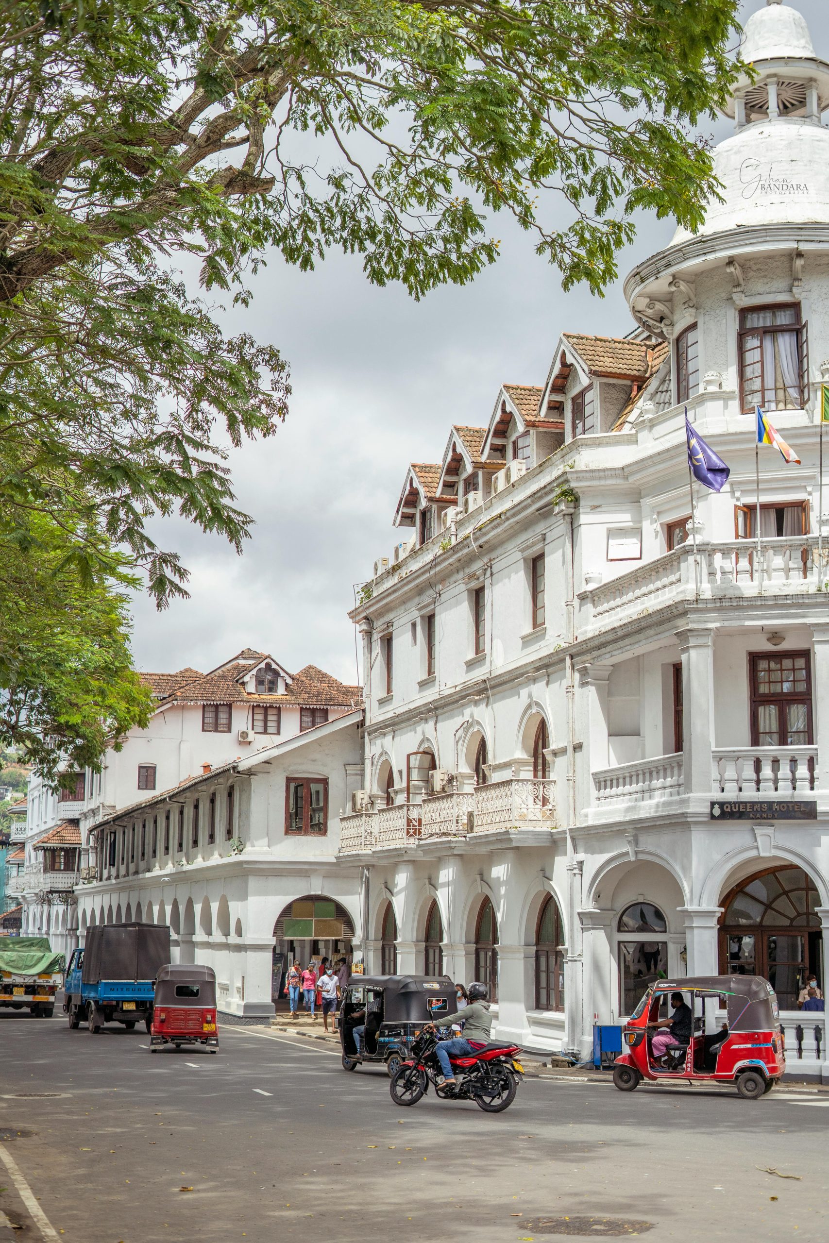 Lively street scene with colonial-era buildings and tuk-tuks in Kandy, Sri Lanka.