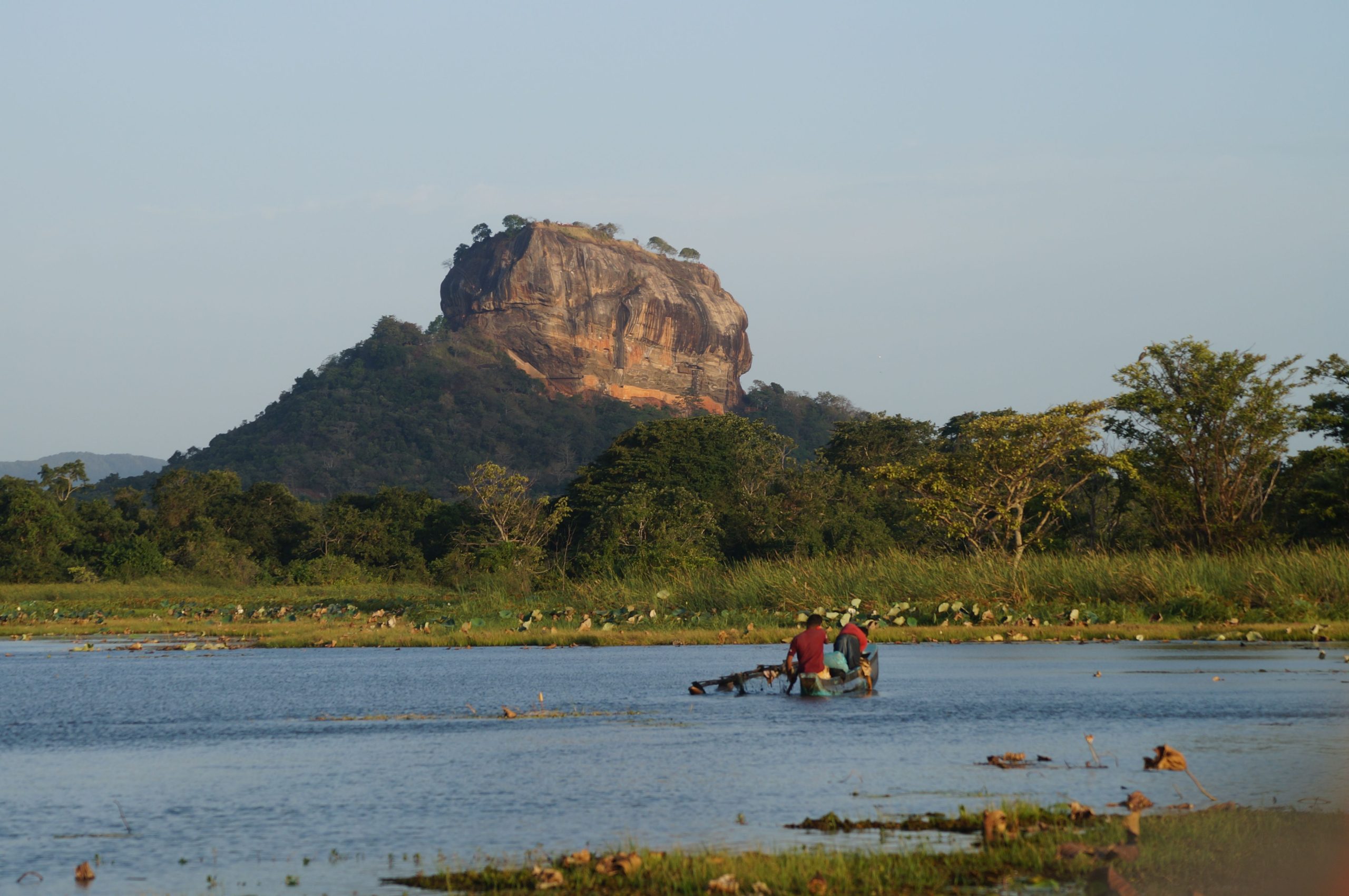 Iconic Sigiriya Rock Fortress with people fishing on a peaceful river in Sri Lanka.