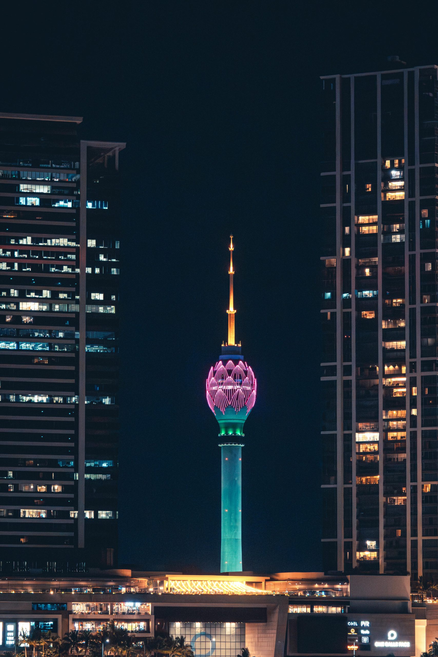 Bright view of Colombo's Lotus Tower at night, glowing in vibrant colors amidst skyscrapers.